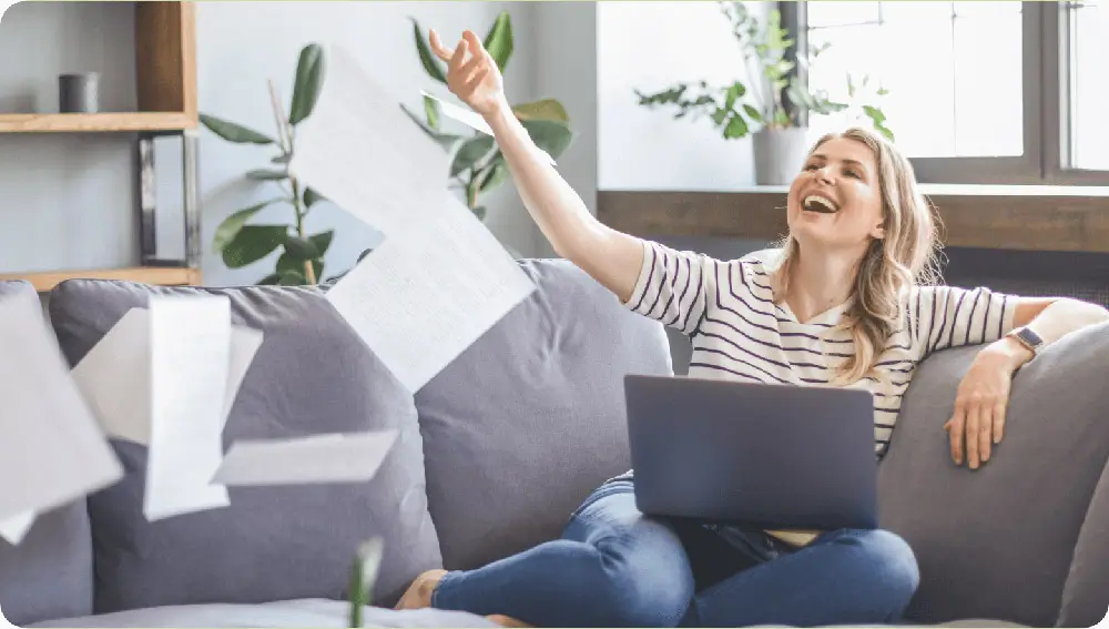 Smiling female sitting on couch throwing documents in the air